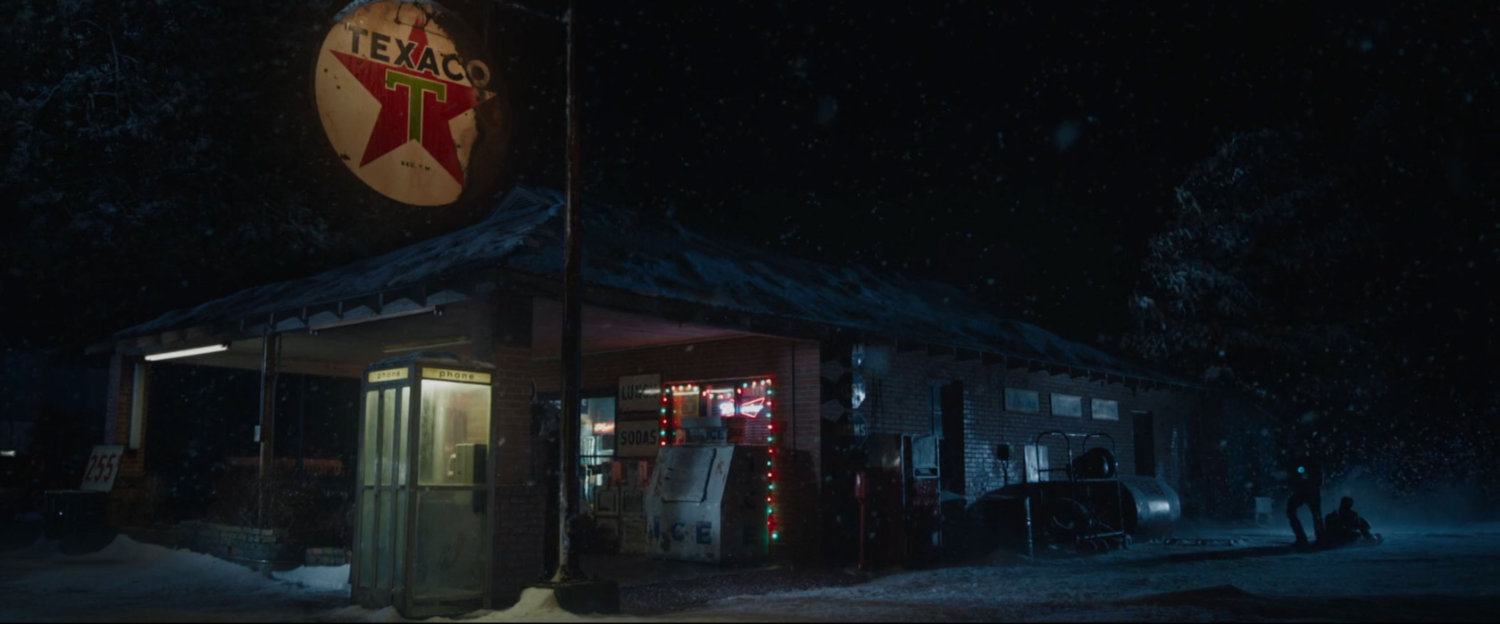 Exterior of a Texaco station at night, as Tony drags his armor through the snow.
