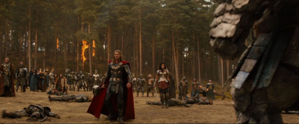 Thor and Asgardian soldiers stand before a tree lined hill.