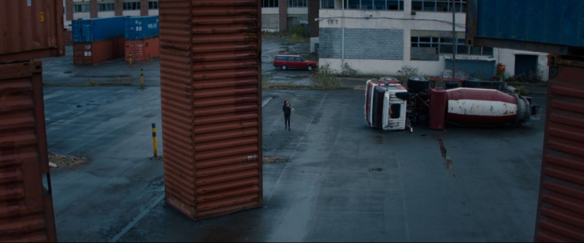 A parking lot with a cement truck on it's side and a vertical storage container.