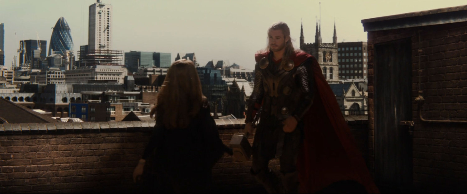 Thor and Jane on a balcony with London buildings in background.