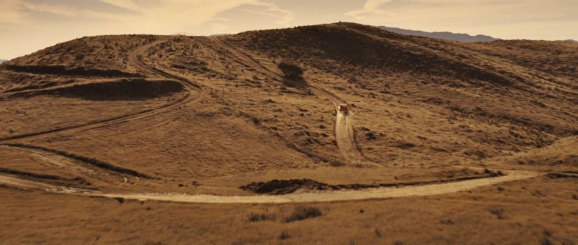 A pickup truck drives over a desert hill.