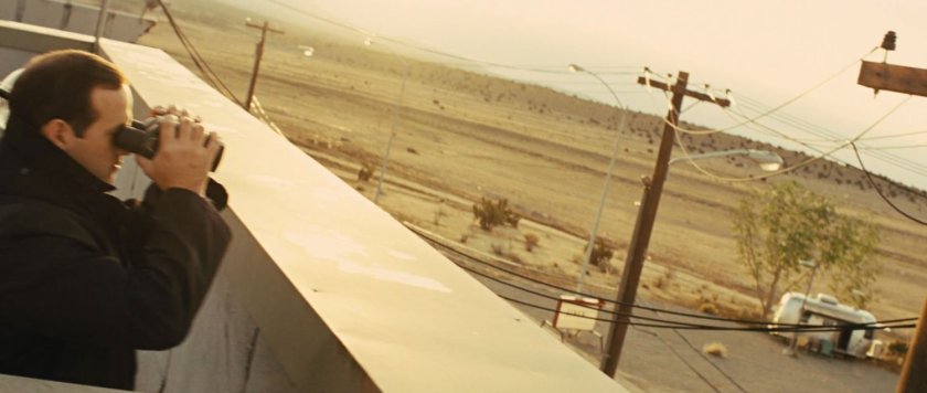 Agent with binoculars on top of Puente Antiguo building looking at desert.