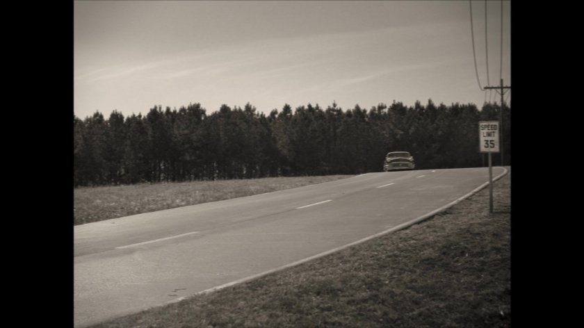 1950s car coming over a small hill on a road.