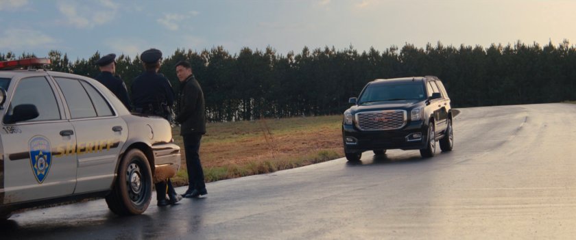 Jimmy Woo and two police officers with Black SUV approaching on road.
