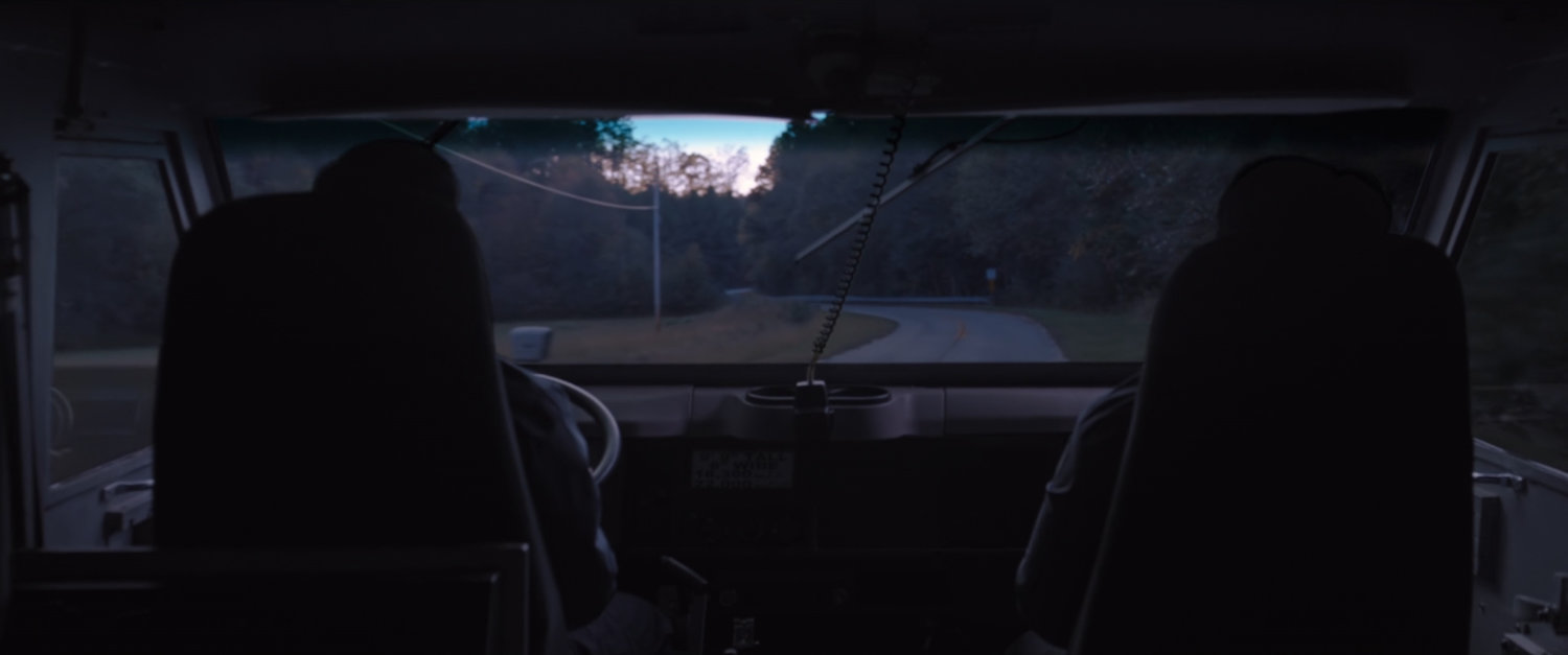 Interior POV from armored truck on dusky road.