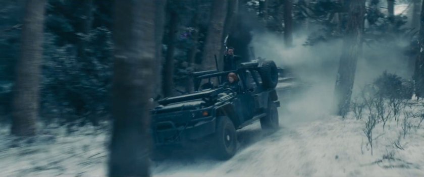 Black Widow and Hawkeye drive a jeep through snowy woods.