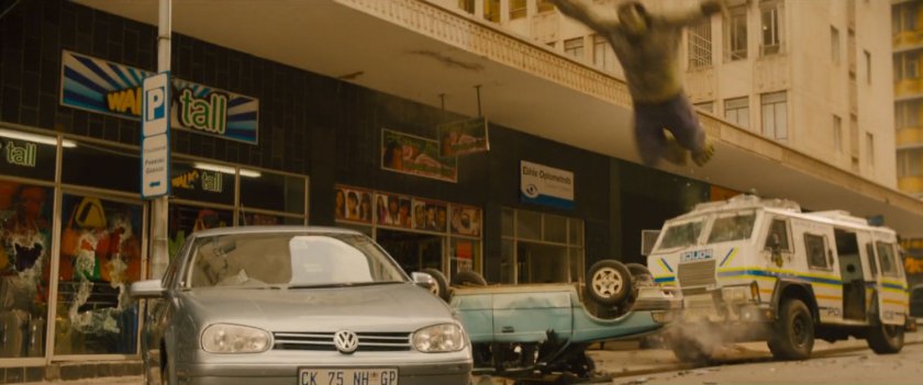 The Hulk leaps of a car in front of a storefront.