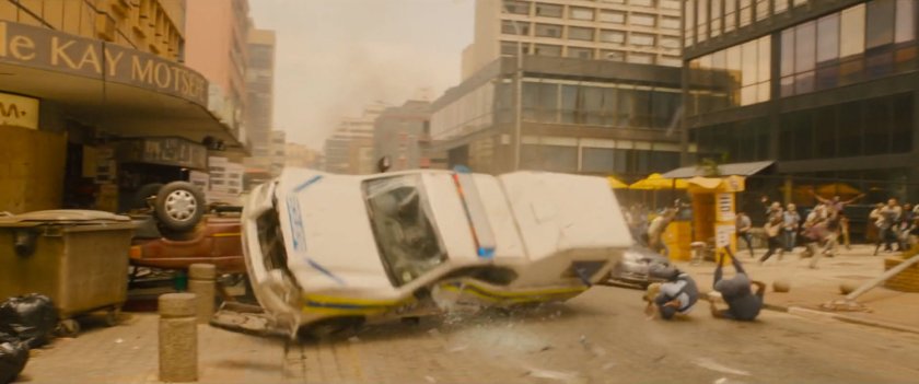 Overturned car and debris in a street as civilians flee.
