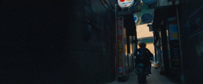 The Black Widow on a motorcycle speeds through a narrow alley.