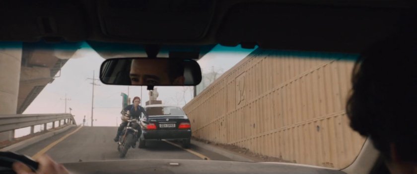 Black Widow rides her motorcycle down a ramp towards oncoming car.