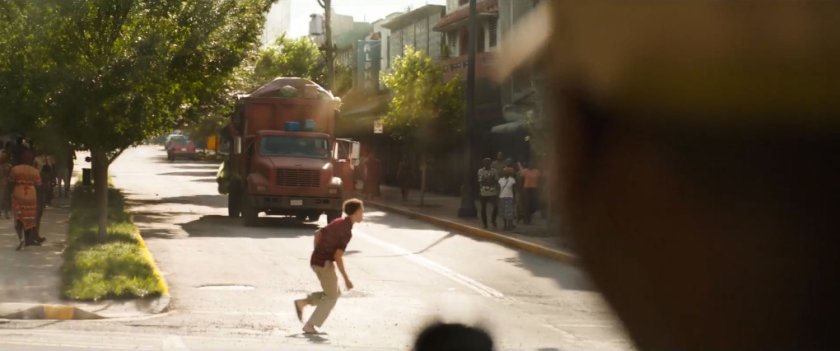 Garbage truck driving on street in Lagos towards boy crossing street.