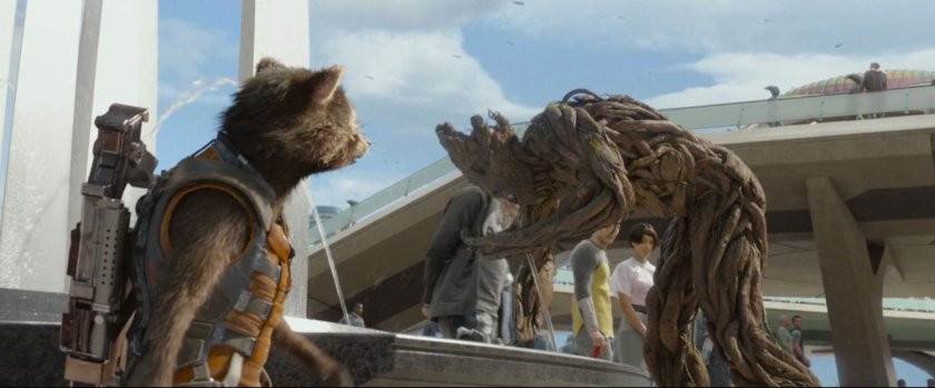 Rocket Racoon talking to Groot, who is drinking out of a fountain in the Xandar plaza.