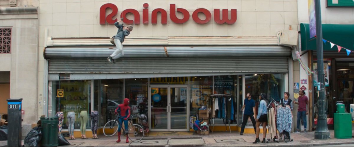 Spider-Man stands in front of a Rainbow store while a webbed bike thief dangles overhead.