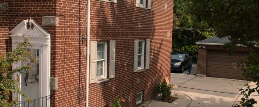 Man walking to car in parking area behind brick building.