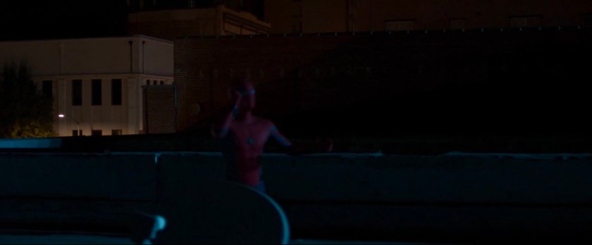 Spider-Man on roof at nighttime taking a phone call.