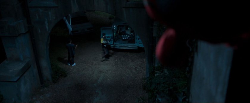 Spider-Man looking down at two men and weapons in the back of a van.
