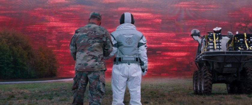 Monica in a spacesuit getting instructions from military man, with red sky in background.