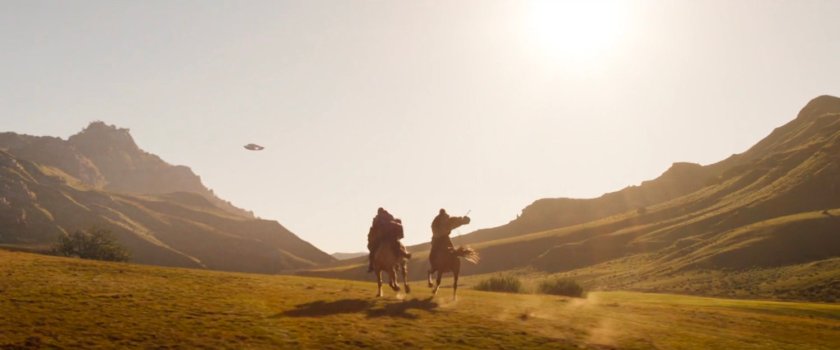 Two men on horseback ride across a hilly farm in Wakanda.
