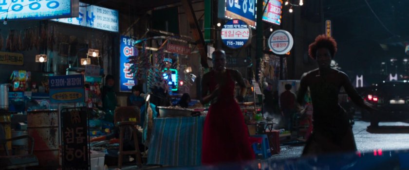 Okoye and Nakia running through a Busan alley/market.