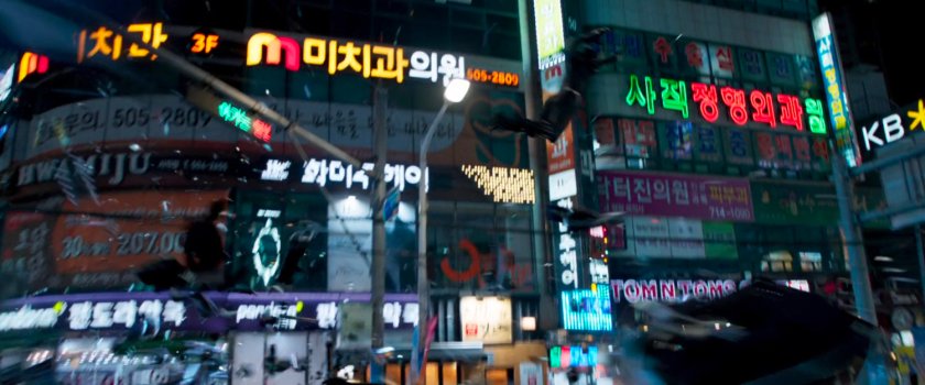 Black Panther jumps through the air in front of brightly lit signs in Busan.