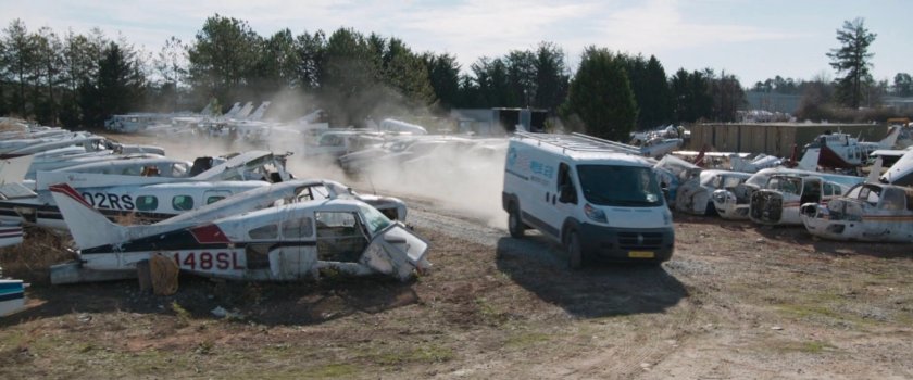 A white van drive through an airplane graveyard.