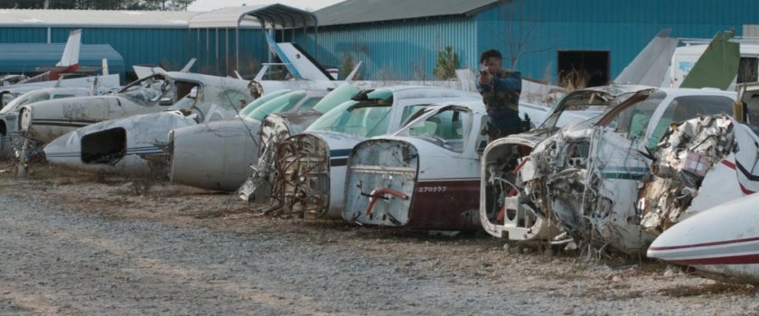 Killmonger fires a gun while standing by airplane parts.
