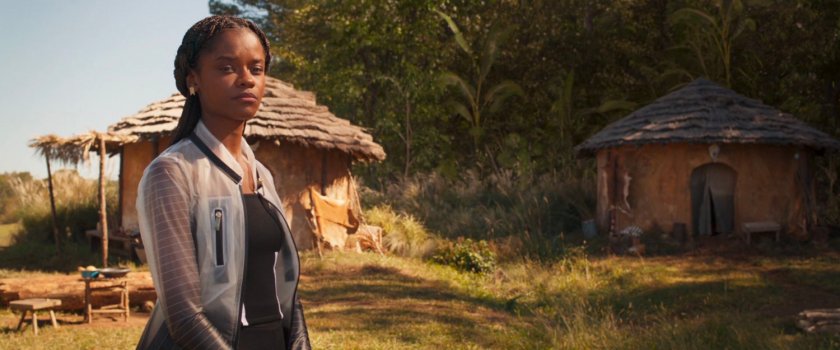 Shuri standing in front of River Tribe huts.
