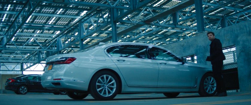 Bucky standing by car in futuristic parking garage.