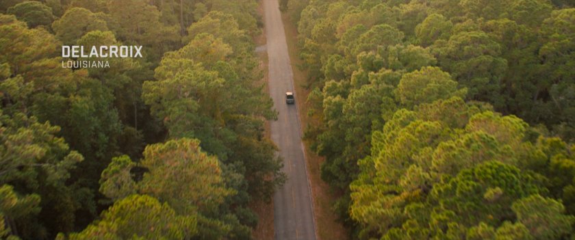A car on a tree lined highway. Text: Delacroix Louisiana.