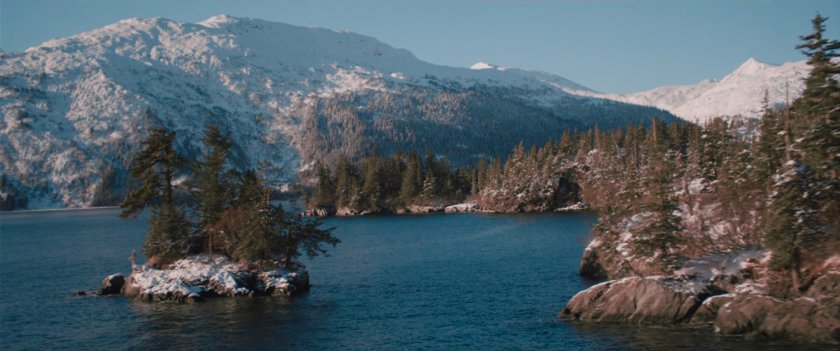 A small snowy island in a lake by Alpine mountains and forest.