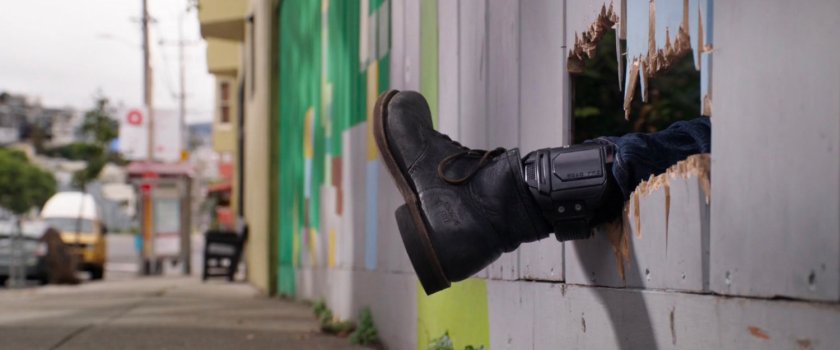 Foot with tracker sticking through wooden fence by sidewalk.