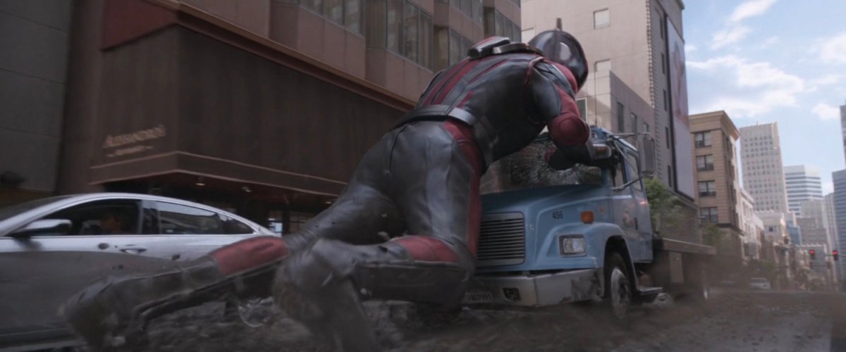 Giant-Man pushing on front of flatbed truck to stop it.