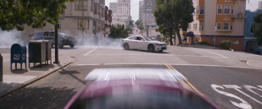 Two cars screech around a corner following a purple car on a San Francisco street.