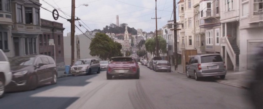 Cad driving on San Francisco street with Coit Tower in distance.