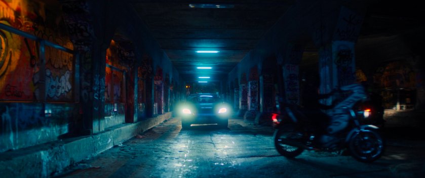 A sedan driving through a graffiti painted tunnel in Madripoor.