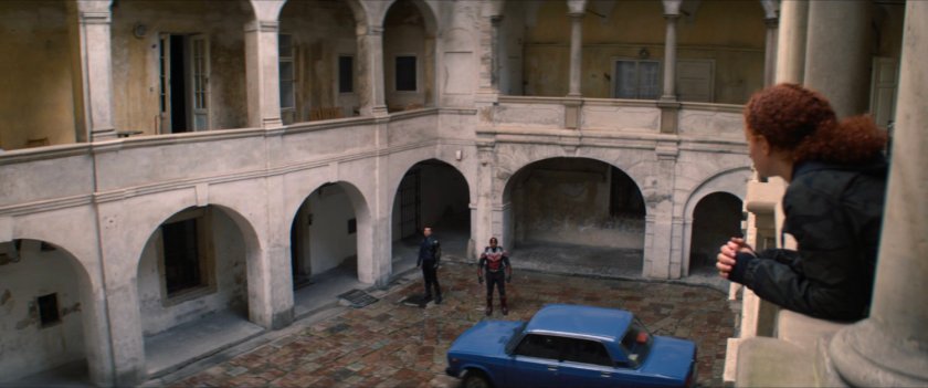 Karli on a balcony talking to Sam and Bucky in a Latvian courtyard.