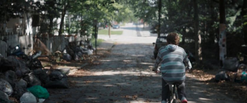 A boy on a bicycle on a dirty residential street.