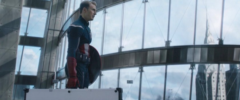 Captain America carrying a case with glass windows behind him.