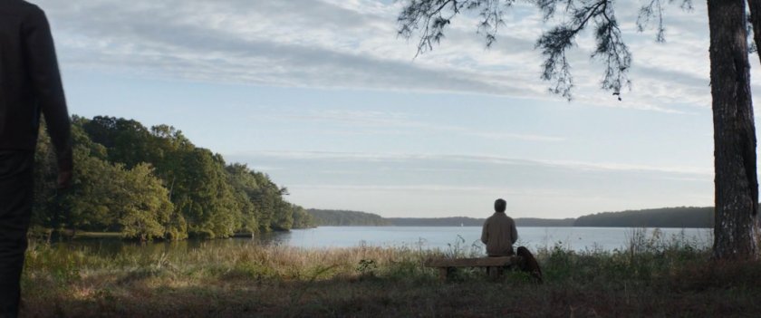 A lone figure sitting on a bench near a lake.