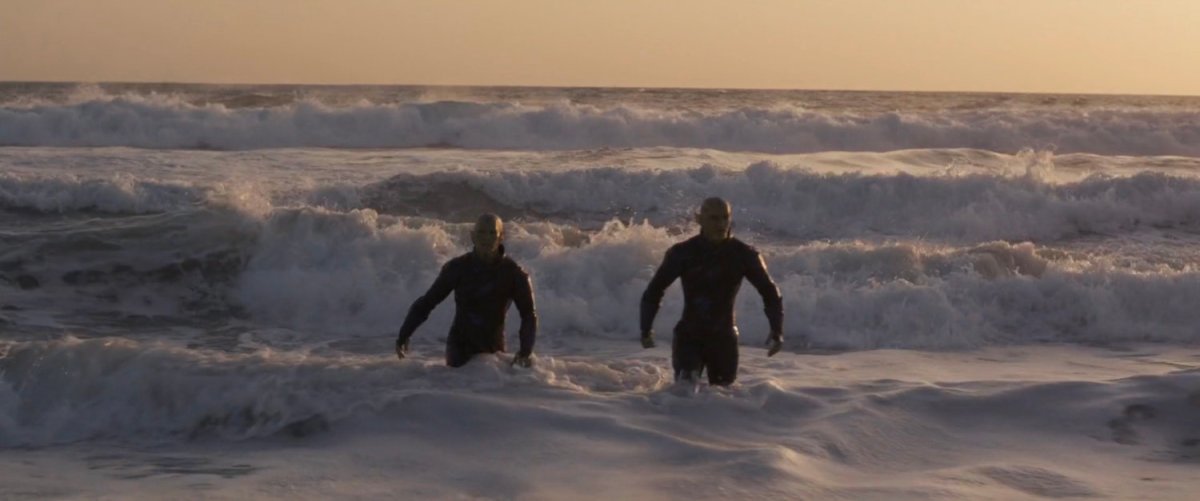Two Skrulls walk out of the surf at a beach.