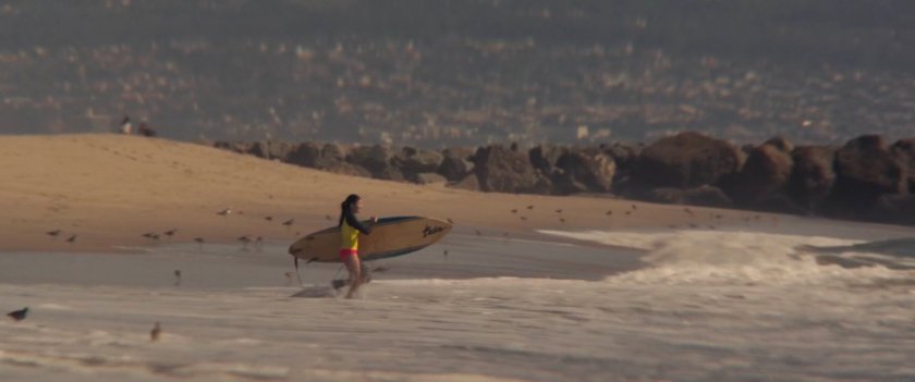A female surfer with her board walking into the ocean.