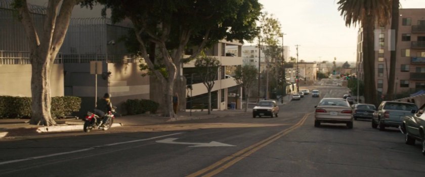 Vers drives away from strip mall on motorcycle.