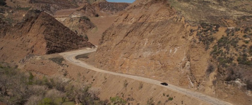 Aerial of car driving along dirty mountain road.