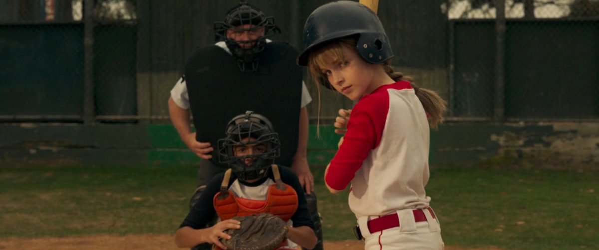 Young Carol Danvers at home plate with a bat during baseball game.