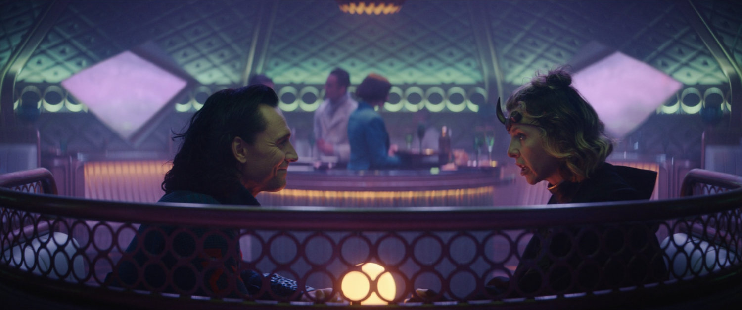 Loki and Sylvie in bar car on train.