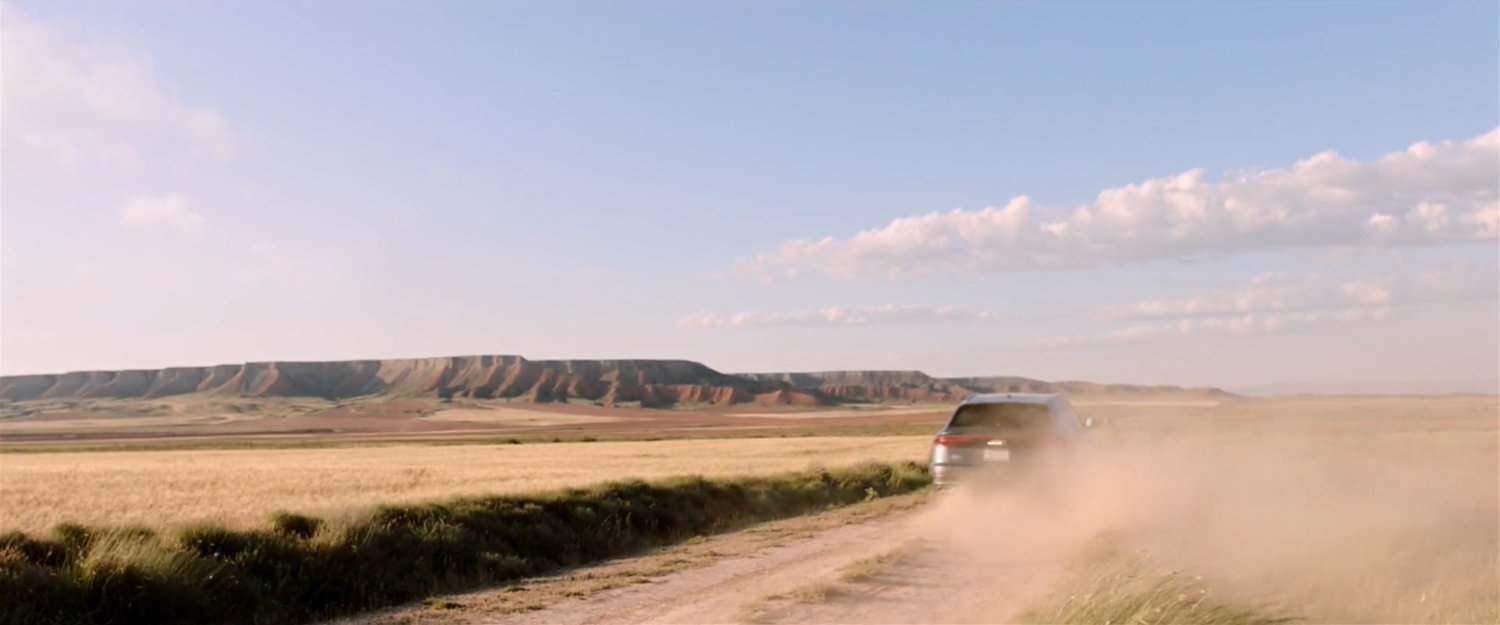 A car driving along a dusty road with a plateau in background.