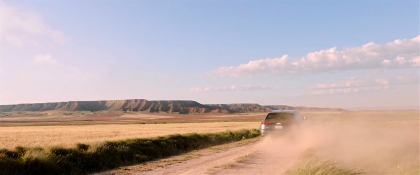 A car driving along a dusty road with a plateau in background.