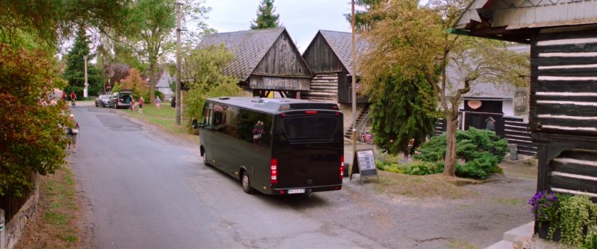 Tour bus pulls into a small rest stop with wooden buildings.