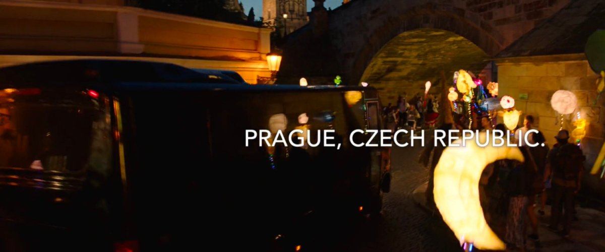 Black tour bus driving under small bridge at night. Text: Prague Czech Republic.