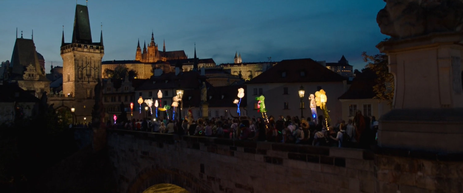 Night time view of Prague with revelers crossing a small bridge.